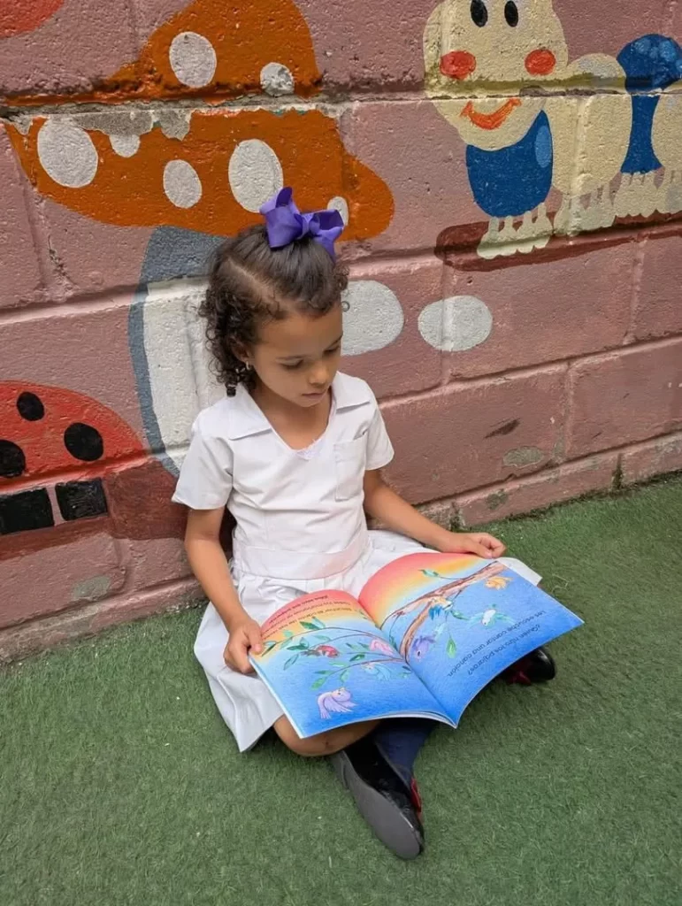 Young child sits outdoors reading an illustrated book.